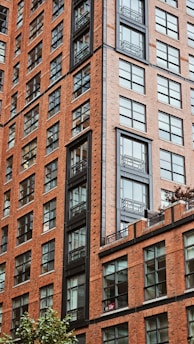 A tall and detailed brick apartment building with numerous windows, featuring modern metal accents and railings. The structure showcases an urban architectural design with clear symmetry and sharp lines.