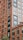 A tall and detailed brick apartment building with numerous windows, featuring modern metal accents and railings. The structure showcases an urban architectural design with clear symmetry and sharp lines.