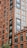 A tall and detailed brick apartment building with numerous windows, featuring modern metal accents and railings. The structure showcases an urban architectural design with clear symmetry and sharp lines.