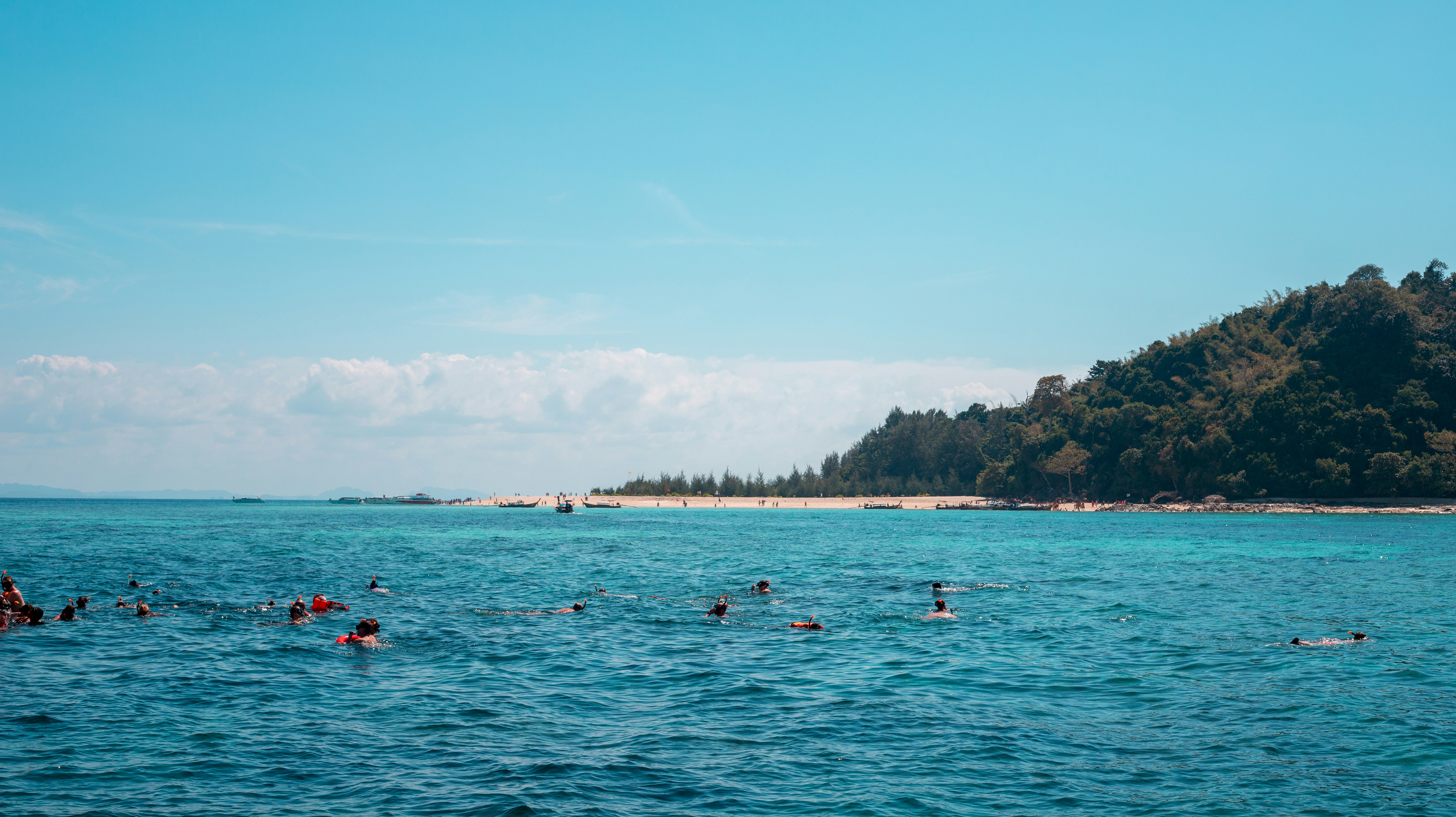 Group of tourists snorkeling in clear turquoise water around coral reef near tropical island