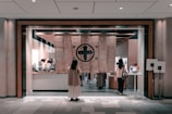 A modern shop interior with large fabric curtains hanging at the entrance featuring traditional symbols. Several people are visible inside, attending to various activities, and there are counters with objects and displays. The overall ambiance suggests a blend of traditional and contemporary styles.
