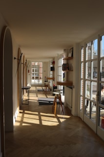 Sunlight streaming through large windows into a shared lounge area filled with books, cushions, and a sense of calm community.
