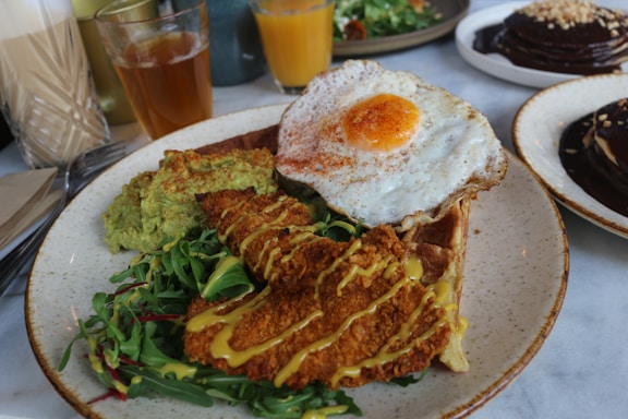 A warm plate featuring crispy golden chicken paired with fluffy waffles, garnished with syrup and fresh herbs.