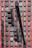 A close-up view of a traffic light system mounted on a pole set against a high-rise building exterior with alternating red and black panels. The traffic lights are black and appear to be in an off state, with visible wires and metal attachments.