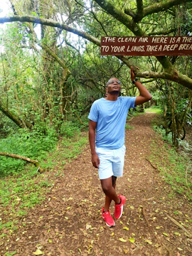 Close-up of a person taking a deep breath outdoors surrounded by green trees and fresh air.