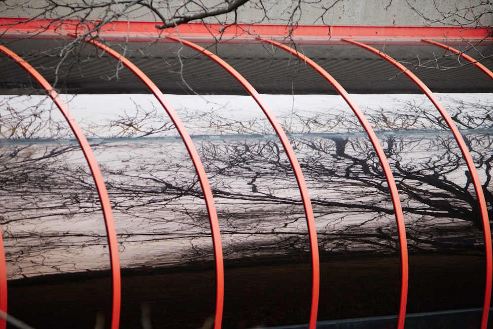 a row of red metal poles sitting next to a tree