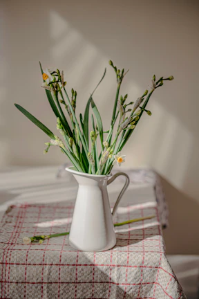 A bright yellow ceramic pitcher filled with fresh flowers, glowing in natural sunlight by a window.