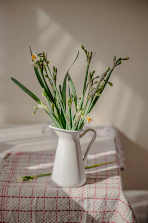 A bright yellow ceramic pitcher filled with fresh flowers, sitting on a rustic dining table.