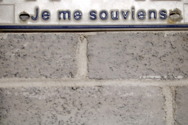 A close-up view of a concrete wall with a metallic plate that has text in French, 'Je me souviens,' which appears to be a motto or slogan. The plate has a simple design.