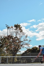 A tennis court with players practicing their serves under a clear blue sky.