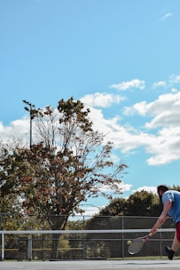 A tennis court with players practicing their serves under a clear blue sky.