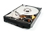 An open hard drive with visible platters, read/write arm, and actuator assembly. The metallic surface appears reflective and detailed, with mechanical components exposed.
