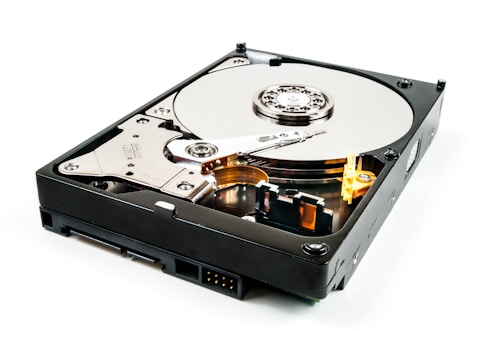 An open hard drive with visible platters, read/write arm, and actuator assembly. The metallic surface appears reflective and detailed, with mechanical components exposed.