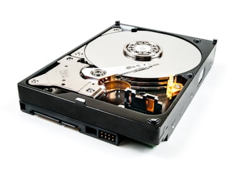 An open hard drive with visible platters, read/write arm, and actuator assembly. The metallic surface appears reflective and detailed, with mechanical components exposed.