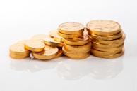 Stack of gold coins shimmering under bright light on a wooden table.