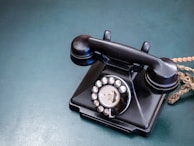 Close-up of a rotary phone with a coiled cord, sitting on a lace doily atop a vintage side table.