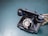 A vintage black rotary telephone with a coiled cord is placed on a flat, textured blue-green surface. The rotary dial is prominently featured, displaying numbers and letters.