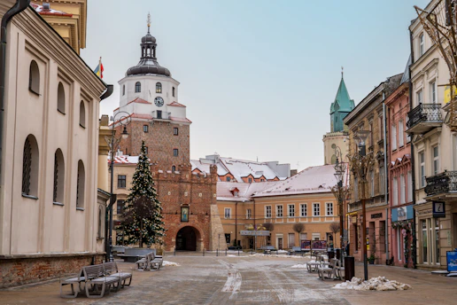 a snowy street with benches and a church in the background