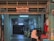 A dimly lit printing works area with a red sign that reads 'Sin & Lee Printing Works' in multiple languages. The entrance is an industrial corridor with fluorescent lighting and various industrial equipment scattered around. A person wearing a headscarf is walking past, captured with motion blur.