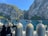 A scenic view featuring several scuba diving tanks on a boat with a backdrop of massive, rugged cliffs covered in patches of green foliage. The clear blue sky and calm water add to the tranquility of the scene.