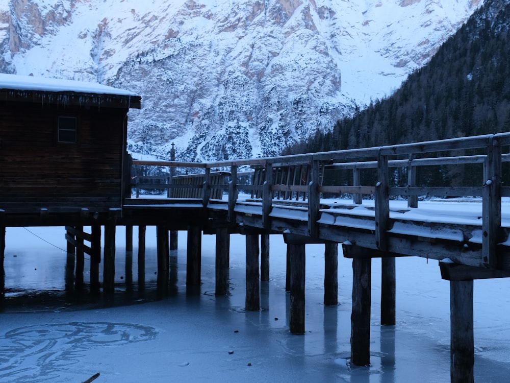 a wooden bridge over a frozen lake with mountains in the background
