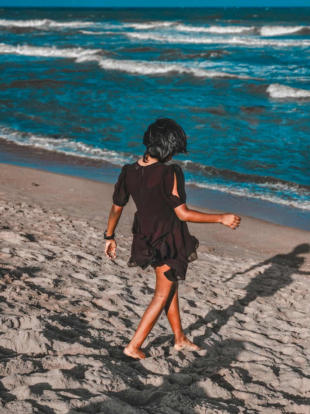 a little girl walking on a beach next to the ocean