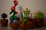 A collection of LEGO plants arranged in brown pots, featuring a variety of colors and designs, including plants with red flowers, a spherical green cactus, and other unique floral shapes.