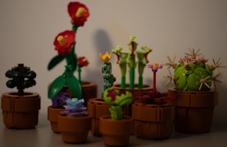 A collection of LEGO plants arranged in brown pots, featuring a variety of colors and designs, including plants with red flowers, a spherical green cactus, and other unique floral shapes.