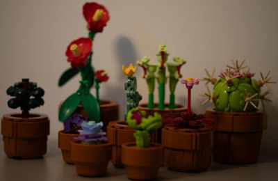 A collection of LEGO plants arranged in brown pots, featuring a variety of colors and designs, including plants with red flowers, a spherical green cactus, and other unique floral shapes.