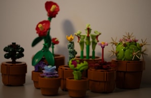 A collection of LEGO plants arranged in brown pots, featuring a variety of colors and designs, including plants with red flowers, a spherical green cactus, and other unique floral shapes.
