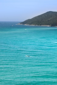 A panoramic view of a turquoise ocean with a small boat drifting near a tropical island.