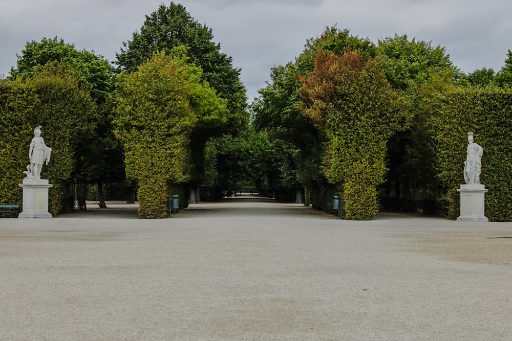 a walkway lined with trees and statues in a park