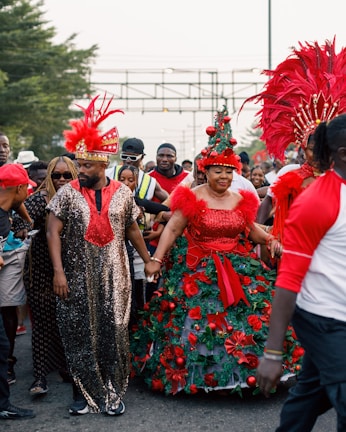 A festive parade with people wearing vibrant and elaborate costumes adorned with feathers and decorations. The scene is lively with a variety of individuals, some wearing sunglasses and hats, creating a cheerful atmosphere.