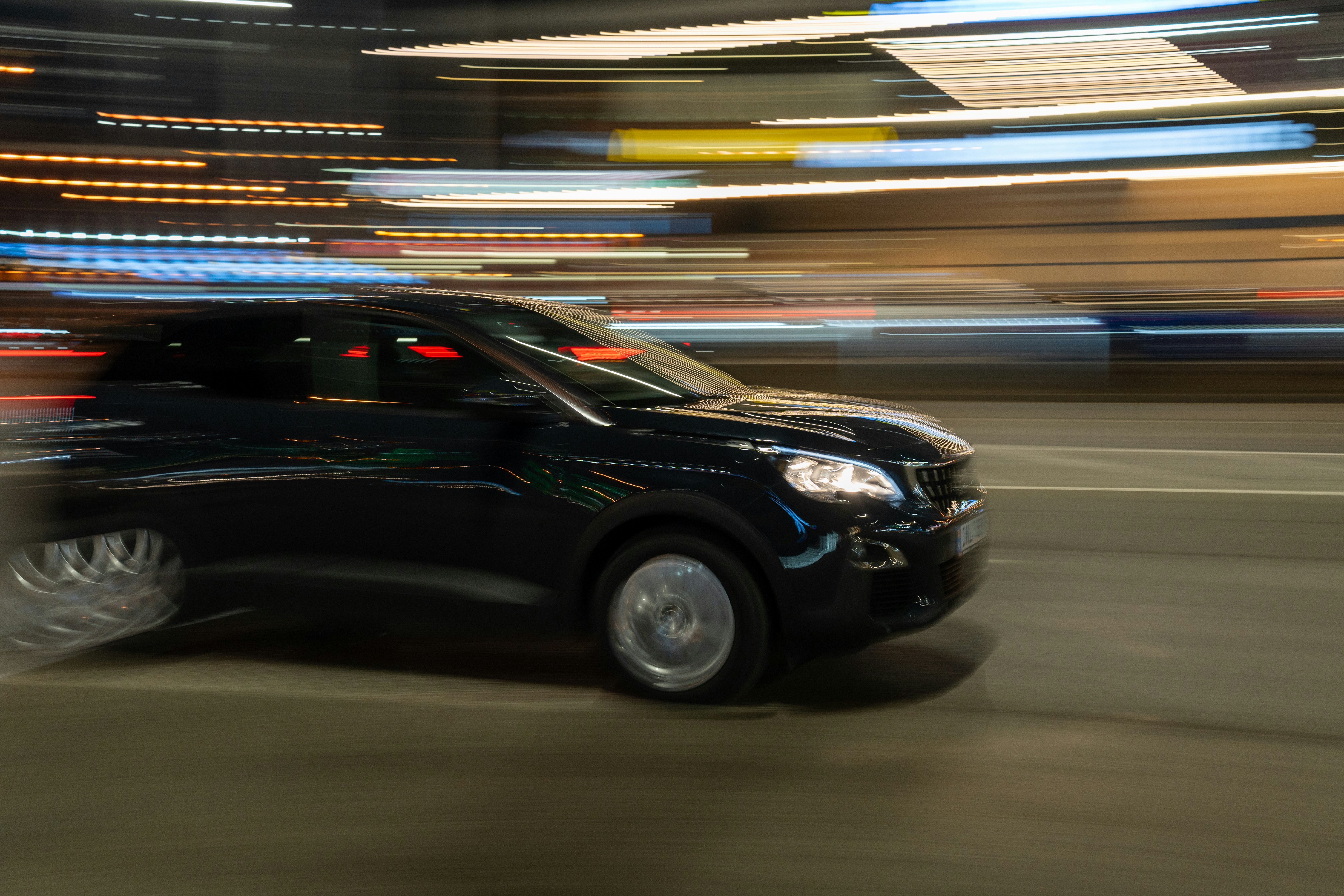 A black car driving down a street at night photo – Free Car Image on ...