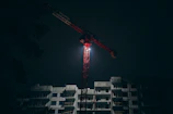 Nighttime operation of a saffron-colored crane illuminating a construction zone in Thane.
