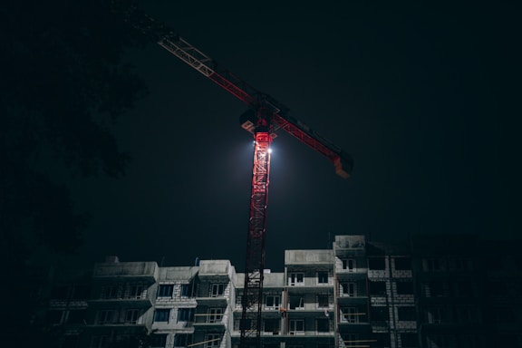 A tall navy blue solar lighting tower illuminating a dark construction site at night.