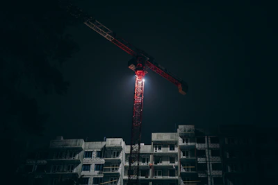 Nighttime operation of a saffron-colored crane illuminating a construction zone in Thane.