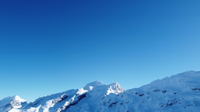 A panoramic view of snow-covered mountain peaks under a clear blue sky.