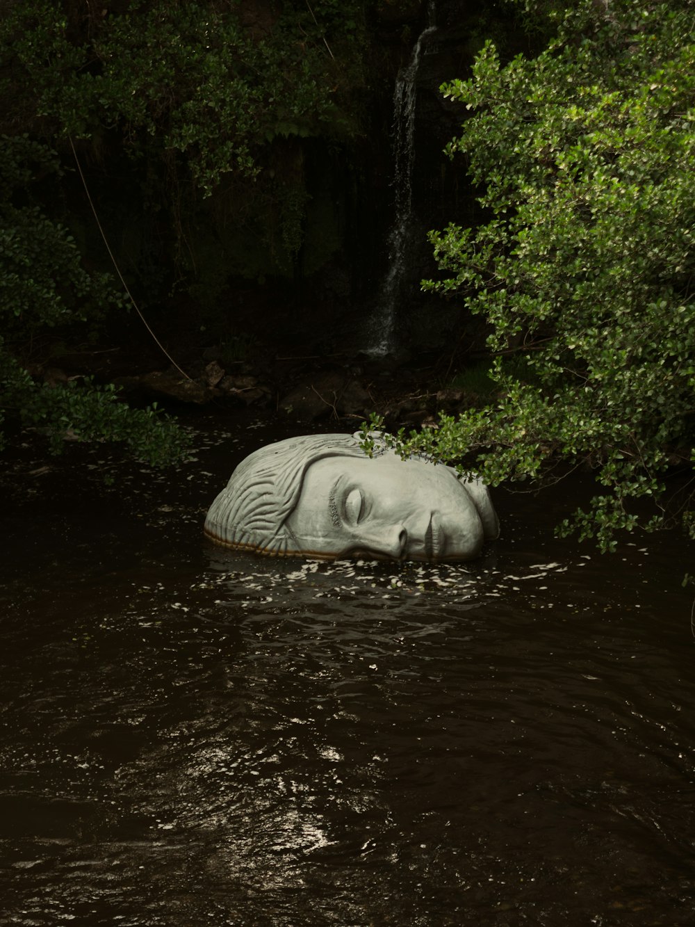 a statue is submerged in the water near a waterfall