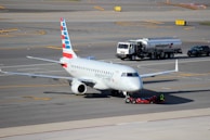 A commercial airplane is being towed on an airport tarmac. The aircraft has American Eagle branding on its fuselage and vertical stabilizer. Nearby, a fuel truck labeled Swissport is stationed, as well as a smaller utility vehicle.