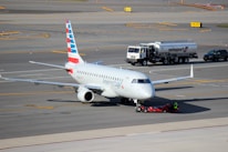A commercial airplane is being towed on an airport tarmac. The aircraft has American Eagle branding on its fuselage and vertical stabilizer. Nearby, a fuel truck labeled Swissport is stationed, as well as a smaller utility vehicle.