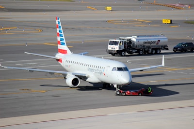 A commercial airplane is being towed on an airport tarmac. The aircraft has American Eagle branding on its fuselage and vertical stabilizer. Nearby, a fuel truck labeled Swissport is stationed, as well as a smaller utility vehicle.