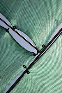 Green mesh fabric stretched across a structure with visible tension lines and metal eyelets, casting shadows and light reflections.