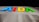 Multicolored letters spelling AIDA are illuminated against a dark background. The letters are vibrant, with blue, red, yellow, and green colors. Below the letters is a section of white material with perforated panels, likely part of a ship or a similar structure.