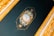 An intricately designed golden frame surrounds a dark background featuring an ornate circular emblem. The emblem includes delicate floral patterns and a central design resembling a compass or clock, crafted with elaborate gold detailing and soft pastel colors.