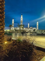 A peaceful evening view of the mosque illuminated, with community members walking nearby.