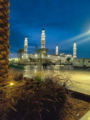 A peaceful evening view of the mosque illuminated, with community members walking nearby.