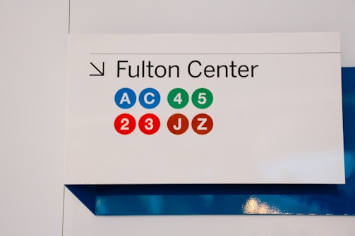 A sign for the Fulton Center is displayed featuring colored circles with letters and numbers, indicating subway lines A, C, 4, 5, 2, 3, J, and Z.