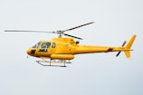 A bright yellow helicopter is flying in the sky, showcasing sleek aerodynamic design with visible registration marks. The helicopter has a single main rotor and a tail rotor.