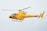 A bright yellow helicopter is flying in the sky, showcasing sleek aerodynamic design with visible registration marks. The helicopter has a single main rotor and a tail rotor.